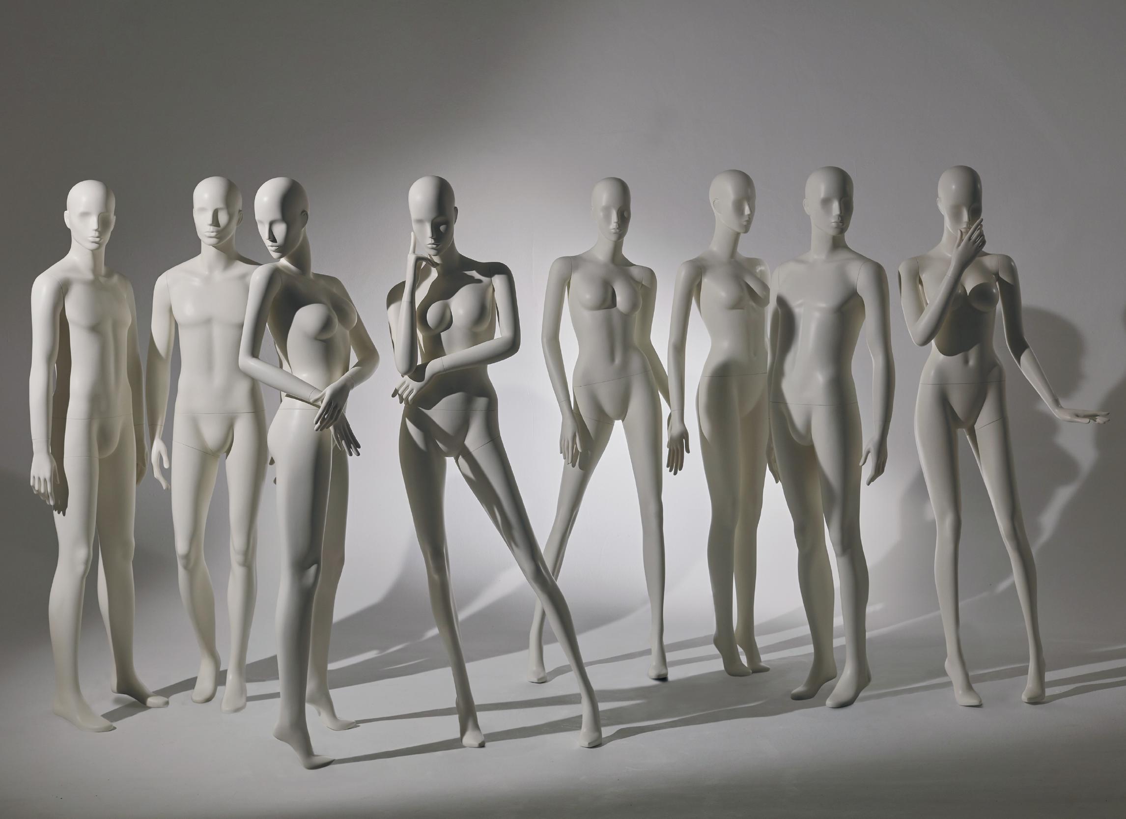 Mannequin by HOL A striking collection of seven white mannequins in various poses stands against a plain grey background. Some are in dynamic stances, with arms bent or raised, while others remain more rigid. The lighting casts shadows, creating a dramatic effect.