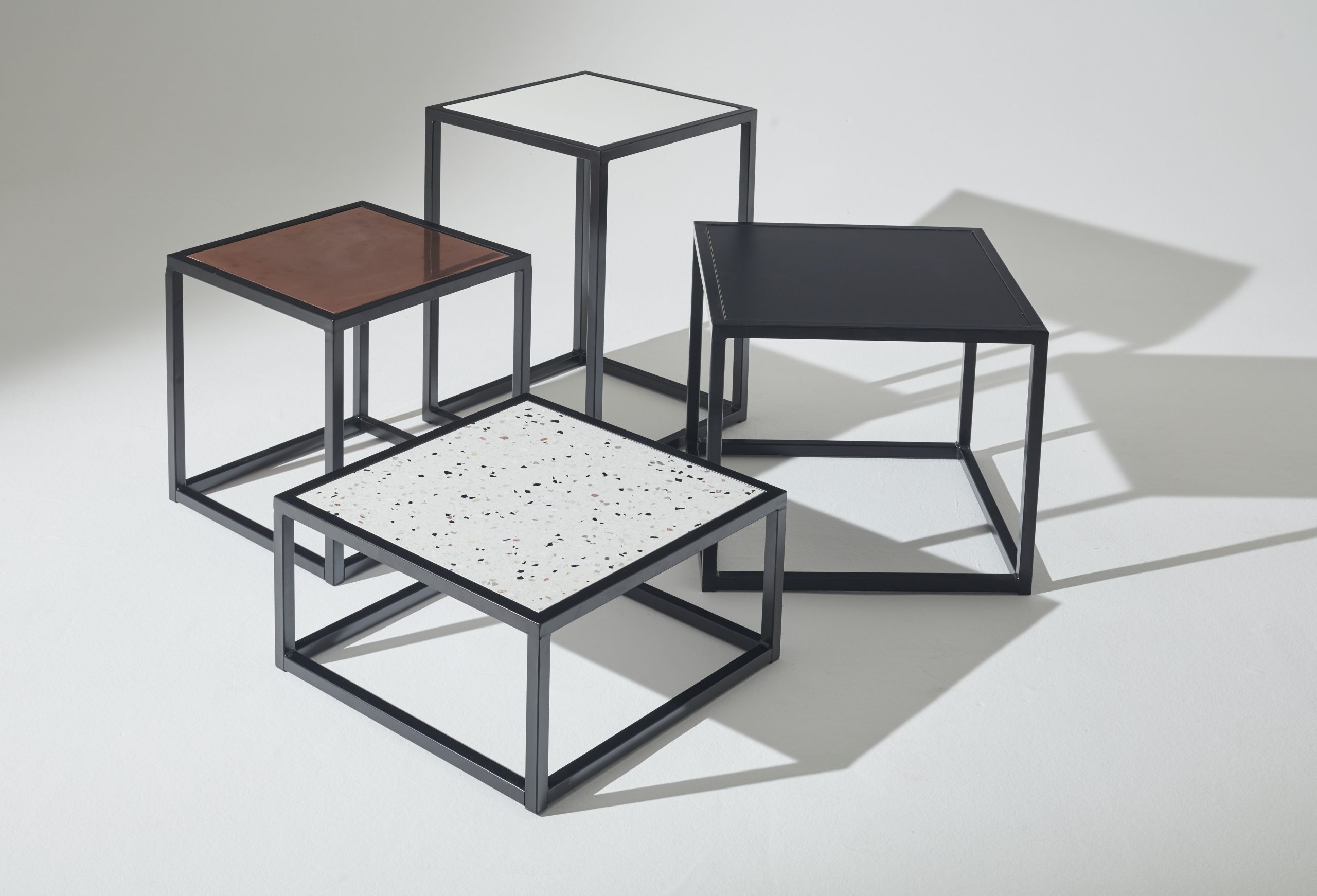 Mannequin by HOL Four minimalist square tables of varying heights and surfaces are arranged on a light background. The tabletops—black, white with speckles, solid white, and brown—are each supported by thin black metal frames. Perfect as props for photoshoots or events, these pieces are available for hire to elevate any space.