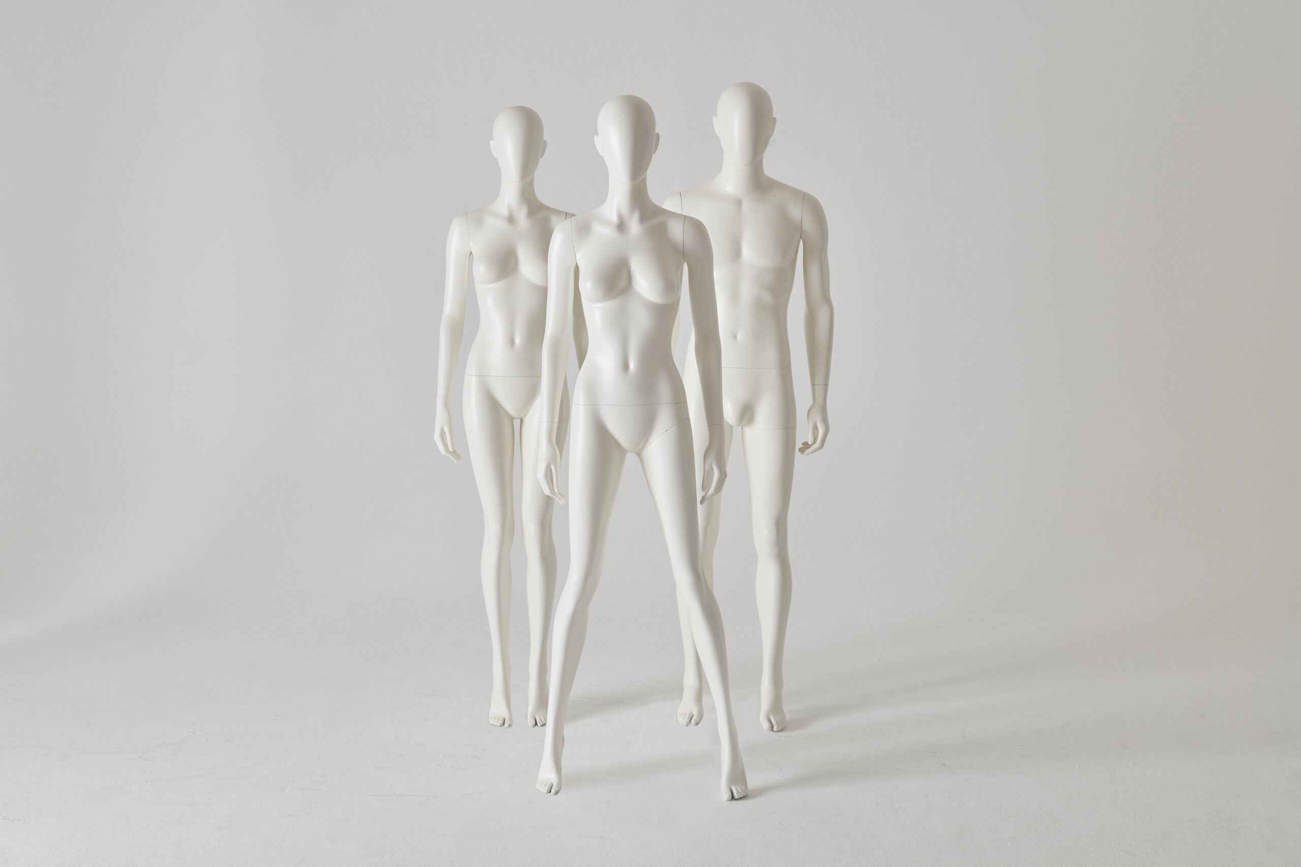 Mannequin by HOL Three white mannequins are posed against a plain gray backdrop. Two female mannequins are positioned slightly in front, with one male mannequin standing behind them. All are featureless and expressionless, resembling a silent collection of human forms.